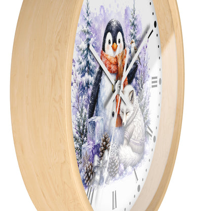 A round wall clock with a light natural wood frame and a white face featuring a winter illustration of a penguin, fox, pine trees, and snow. The clock is shown at an angle against a plain white background.