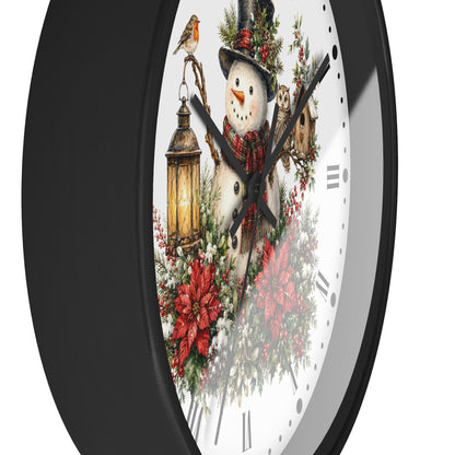 A round wall clock with a black frame and a white face featuring a winter holiday illustration of a snowman, red poinsettias, green foliage, a lantern, birds, and a birdhouse.