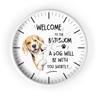 A round white wall clock with black hands and black hour markers, featuring a printed illustration of a beagle dog and the text 'WELCOME TO THE BATHROOM A DOG WILL BE WITH YOU SHORTLY.' on a white background.