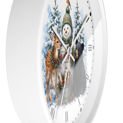 A white round wall clock with a winter woodland illustration on the face, featuring a snowman in a green hat, a deer with a wreath, a bear, snowy trees, and a bird feeder. The clock is shown against a plain white background.