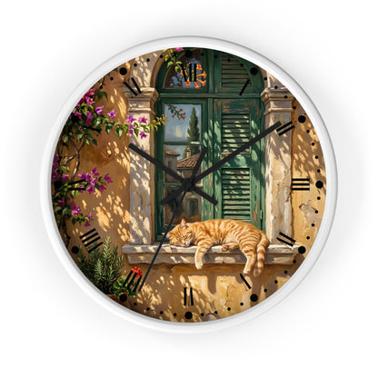 Round wall clock with a white frame and a printed scenic design featuring a green shuttered window, warm beige stucco wall, climbing pink flowers, and an orange tabby cat resting on a windowsill. Black clock hands and black Roman numerals are visible against a plain white background.