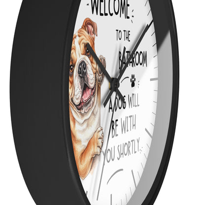 A round wall clock with a black frame and a white face featuring an illustration of a bulldog and the text 'WELCOME TO THE BATHROOM A DOG WILL BE WITH YOU SHORTLY'.