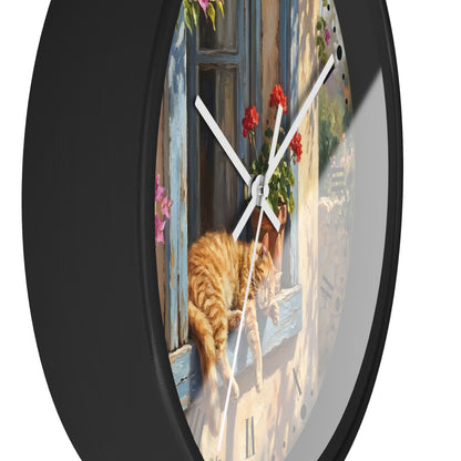 Round wall clock with a black frame and a printed illustration of an orange tabby cat sitting by a blue window with red flowers, shown against a white background.