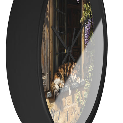 Round wall clock with a black frame and a printed illustration of a calico cat resting on a windowsill next to purple wisteria flowers, shown against a plain white background.
