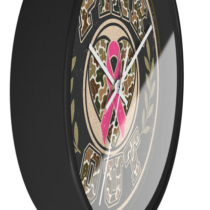 A close-up of a round wall clock with a black frame and a printed dial featuring a pink ribbon over a camouflage heart, with the words 'PINK OUT ' visible.
