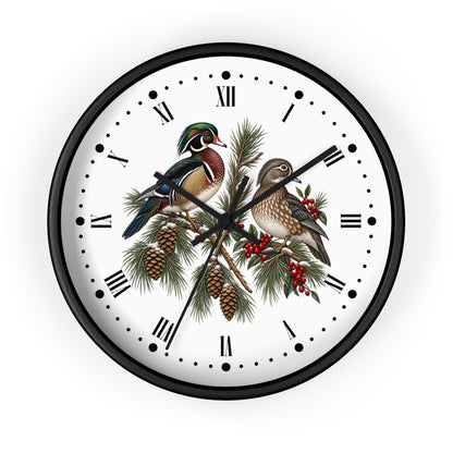 A round wall clock with a black frame and a white face featuring an illustration of two wood ducks perched on pine branches with pinecones and red berries, set against a plain white background.