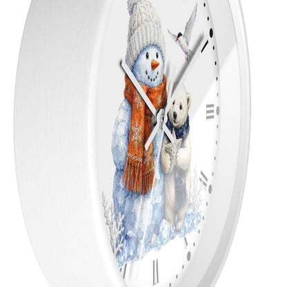 A white round wall clock with a winter illustration on the face, showing a snowman in a cream knit hat and orange scarf next to a white polar bear, with black Roman numerals and white hands.
