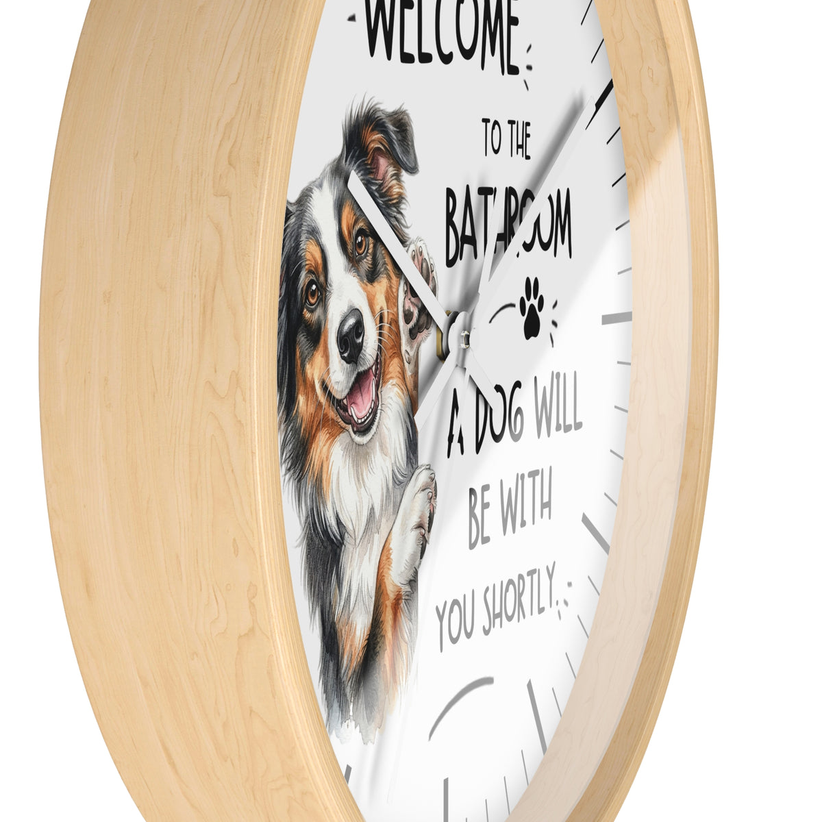 Round wall clock with a light natural wood frame and a white face featuring a watercolor illustration of a tricolor dog and the text 'WELCOME TO THE BATHROOM A DOG WILL BE WITH YOU SHORTLY'.