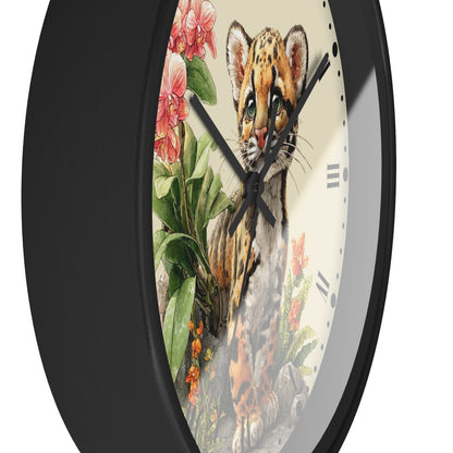 A close-up of a round wall clock with a black frame and a detailed illustration of a spotted cat kitten surrounded by pink flowers and green leaves on the face.