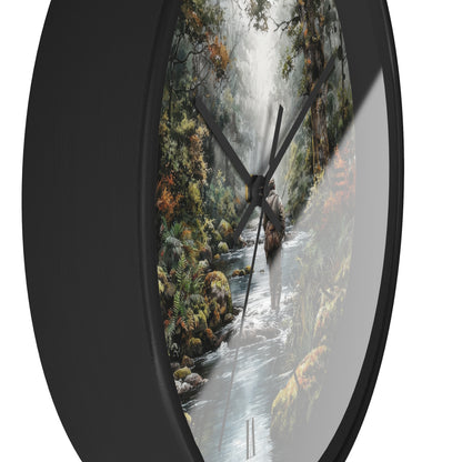 A round wall clock with a black frame and a printed nature scene on the face showing a forest stream, waterfall, and waterfall cascades, photographed against a white background.