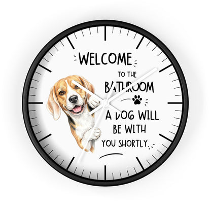 A round wall clock with a black frame and white face, featuring a beagle illustration and the text 'WELCOME TO THE BATHROOM A DOG WILL BE WITH YOU SHORTLY.' on a light gray background.