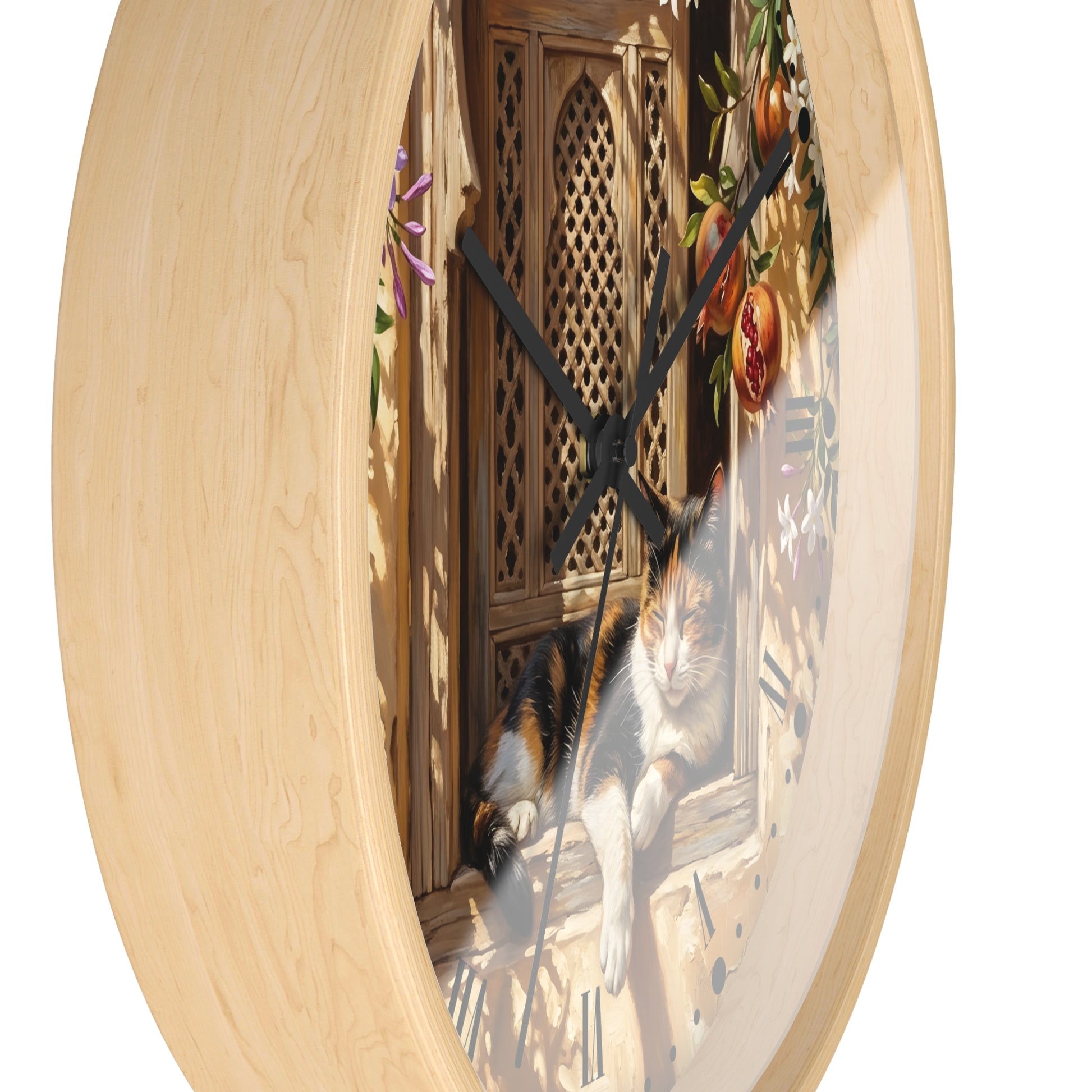 A round wall clock with a light natural wood frame and a printed scene on the face showing a calico cat lounging by a wooden window with hanging fruit and flowers. The clock is photographed against a plain white background.