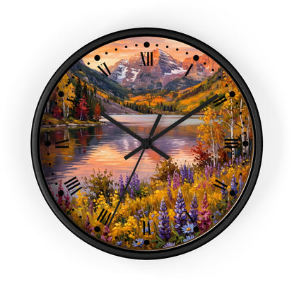 A round wall clock with a black frame and a scenic landscape print featuring a mountain lake at sunset, surrounded by autumn foliage and wildflowers. The clock face has black Roman numerals and black clock hands.