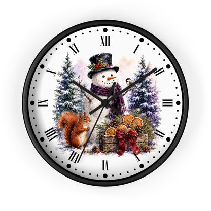 A round wall clock with a black frame and a white face featuring a festive winter illustration. The design shows a snowman in a top hat and scarf, a brown squirrel, evergreen trees, pinecones, and dried orange slices, with black Roman numerals and hour markers.