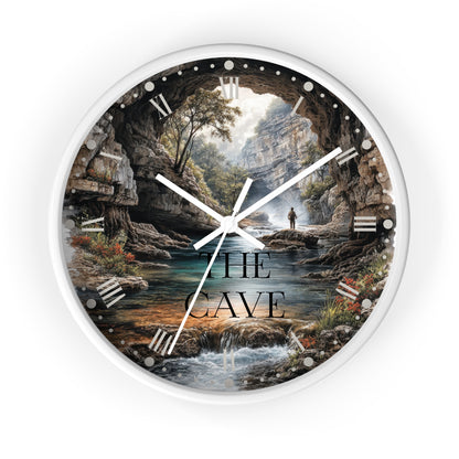 A round wall clock with a white frame and a scenic print of a person standing in a cave overlooking a river and forest. The words 'THE CAVE' are printed on the face.