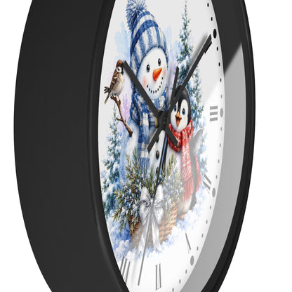 A close-up of a round wall clock with a black frame and a white face featuring a winter holiday illustration of a snowman, a penguin, evergreen trees, and bird perched on the clock hands.