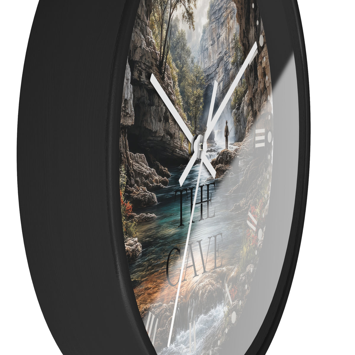 A round wall clock with a black frame and a scenic landscape print showing a cave interior, river, trees, and the words “THE CAVE,” photographed against a white background.