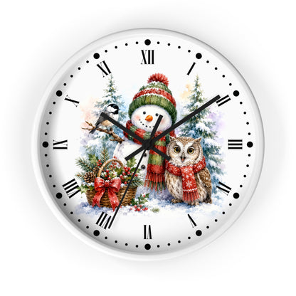 A round wall clock with a white face and outer rim, featuring a festive Christmas illustration with a snowman in a red and green hat and scarf, an owl in a red scarf, evergreen trees, and a basket. The clock uses black Roman numerals and black hands on a white background.