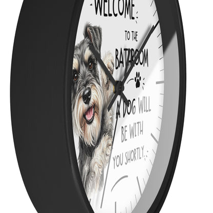 A round wall clock with a black frame and a white face featuring a detailed illustration of a grey and white dog and the humorous text 'WELCOME TO THE BATHROOM A DOG WILL BE WITH YOU SHORTLY'.