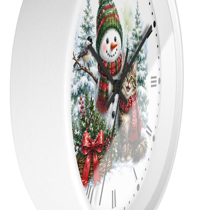 A white round wall clock with a festive winter illustration on the face, showing a snowman in a green and red striped hat and scarf alongside a tabby cat in a red scarf, with black Roman numerals and black hands.