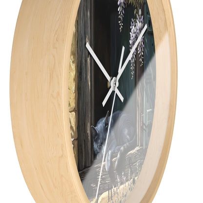 Round wall clock with a light natural wood frame and a printed center scene showing a gray cat near a dark doorway with wisteria flowers. The clock is photographed on a plain white background.