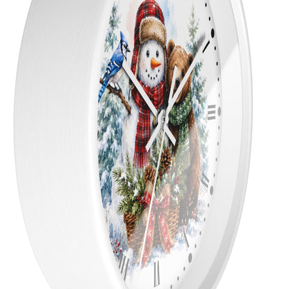 A white round wall clock featuring a festive winter illustration with a snowman in a red plaid scarf, a blue jay, pine trees, and a brown bear, shown against a plain white background.