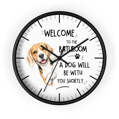 A round wall clock with a black frame and white face, featuring a beagle illustration and the text 'WELCOME TO THE BATHROOM A DOG WILL BE WITH YOU SHORTLY.' on a light gray background.