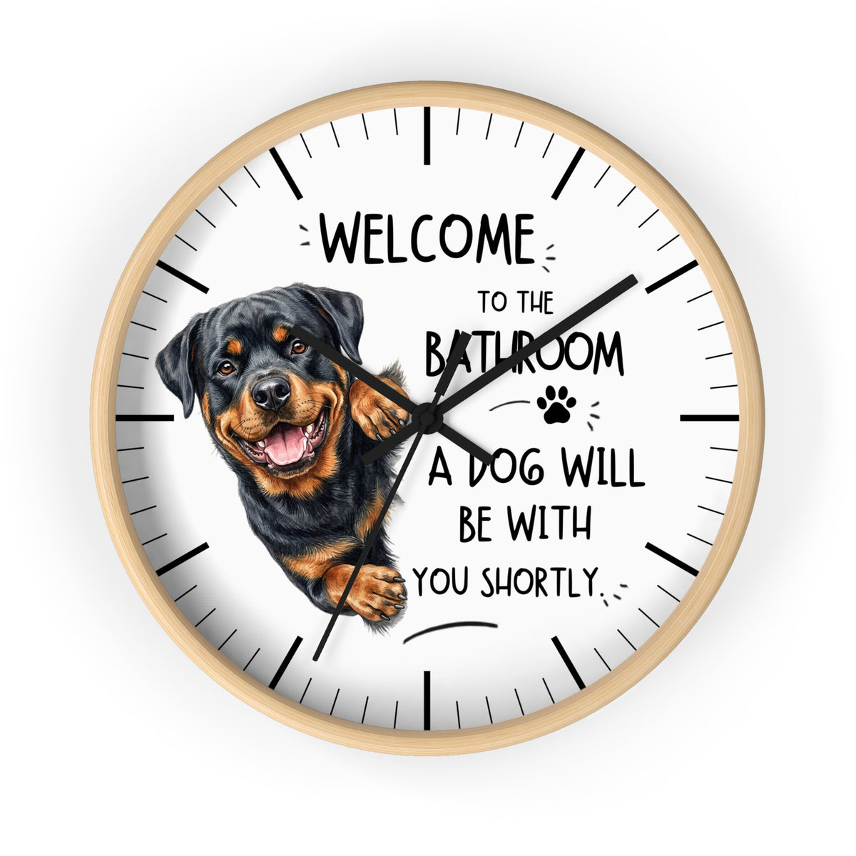 A round wall clock with a white face, black hands, black hour markers, and a printed illustration of a Rottweiler dog next to the humorous text, 'WELCOME TO THE BATHROOM A DOG WILL BE WITH YOU SHORTLY.'.