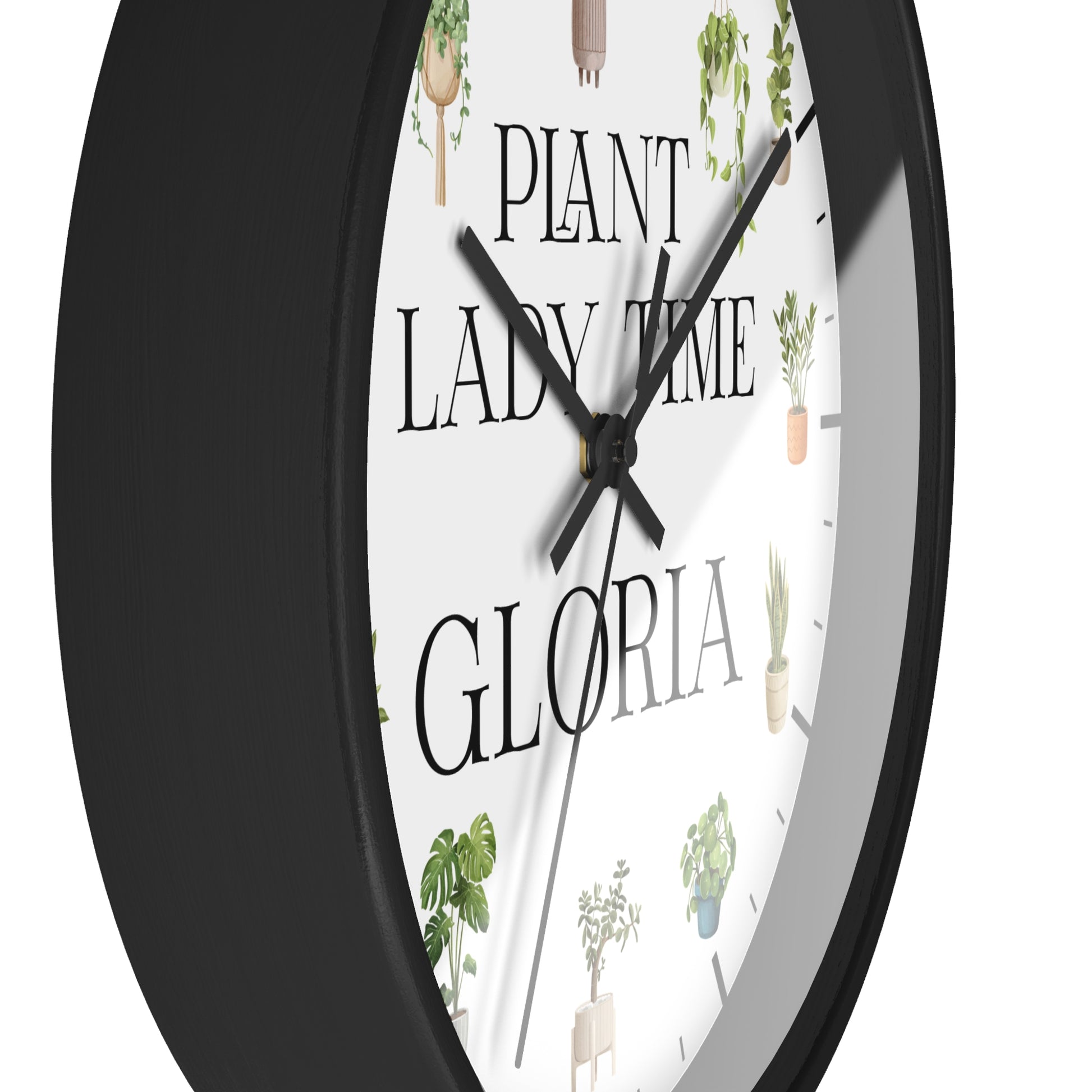 A close-up of a round wall clock with a black frame and a white face featuring the text 'PLANT LADY TIME GLORIA' and small potted plant illustrations.