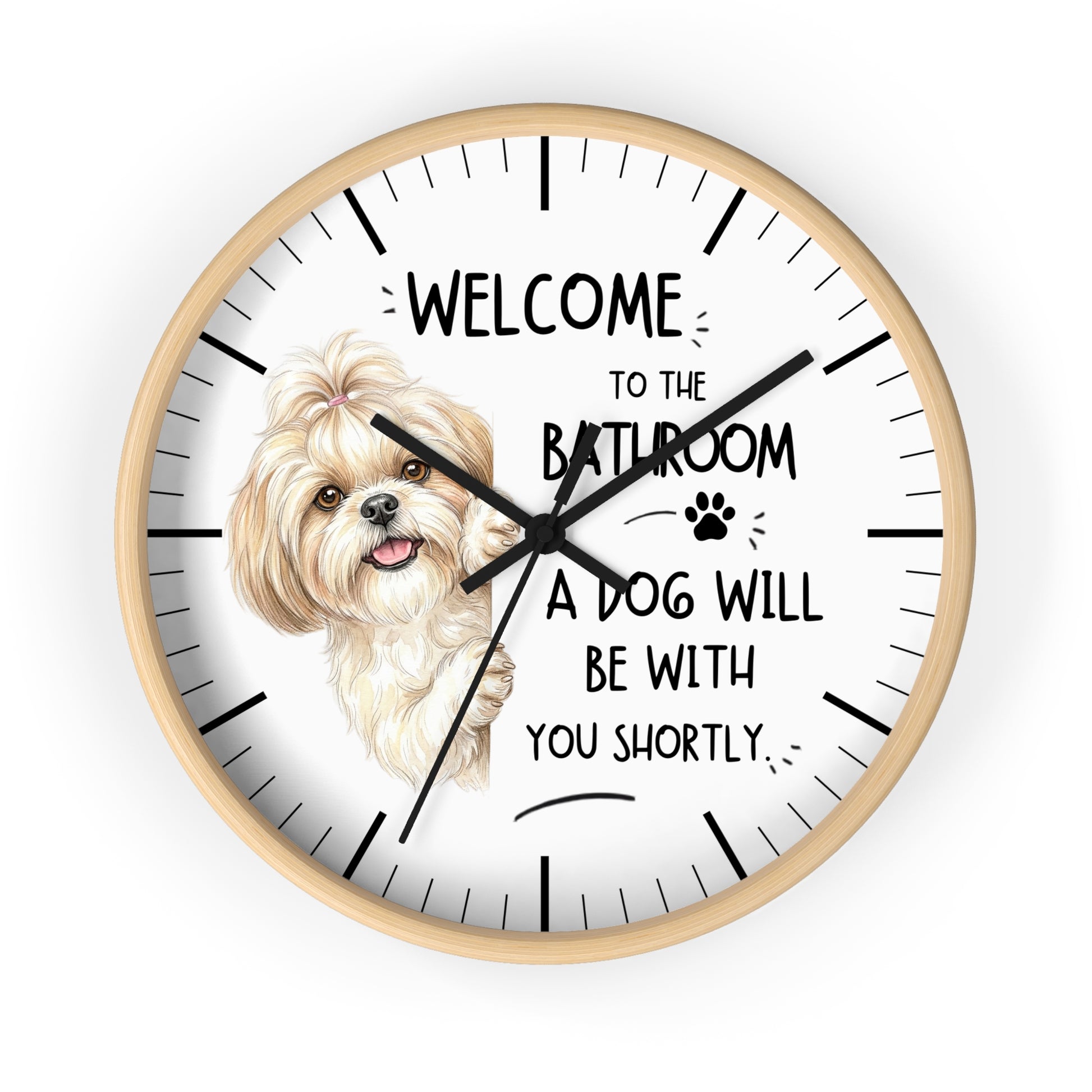 A round wall clock with a light wood frame and a white face, featuring a small fluffy cream-colored dog illustration and the text 'WELCOME TO THE BATHROOM A DOG WILL BE WITH YOU SHORTLY.' The clock is shown against a plain white background.