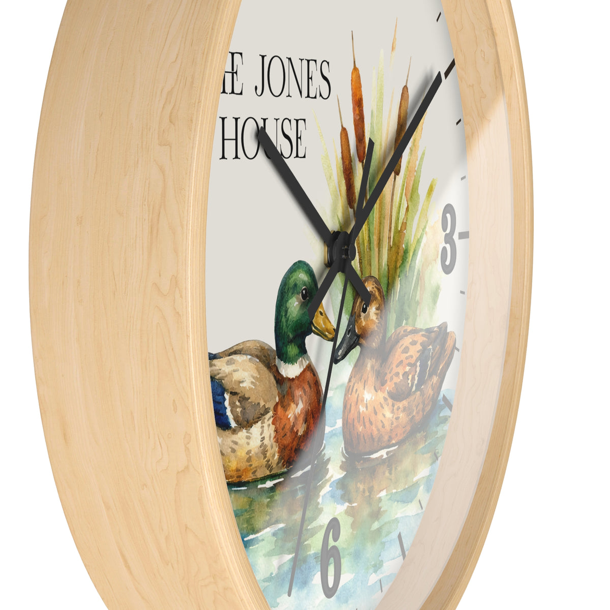 Round wall clock with a light natural wood frame and a printed dial featuring two ducks, cattails, and the text 'THE JONES HOUSE'.