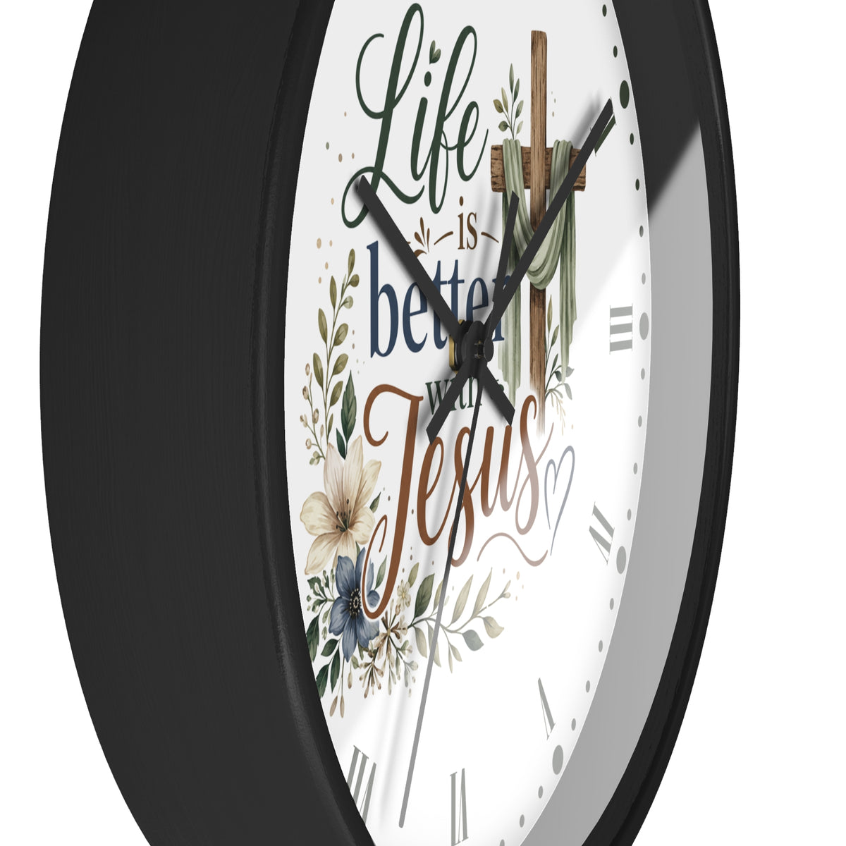 A close-up of a round wall clock with a black frame and a white face featuring the phrase 'Life is better with Jesus' in decorative script, along with floral and cross illustrations.