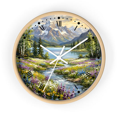 A round wall clock with a light wood frame and a scenic landscape print featuring mountains, a lake, trees, and a wildflower meadow. The clock face has black Roman numerals and white hands, shown against a plain white background.