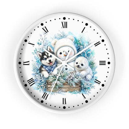 A round wall clock with a white face and outer rim, featuring a winter illustration of a snowman, a husky, a seal, evergreen branches, and a wooden crate. The clock uses black Roman numerals and dot hour markers with white hands.