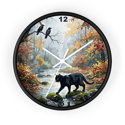 Round wall clock with a black frame and a printed autumn forest scene on the face, featuring a black cat in the foreground, two crows on branches, a stream, and white clock hands. 