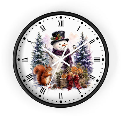 A round wall clock with a black frame and a white face featuring a winter holiday illustration of a snowman, a squirrel, evergreen trees, and gift baskets. The clock uses black Roman numerals and black hour markers.