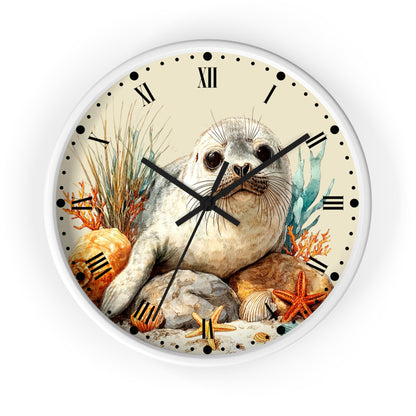 Round wall clock with a white frame and a printed illustration of a seal pup on an ocean beach background, featuring Roman numerals and black clock hands.