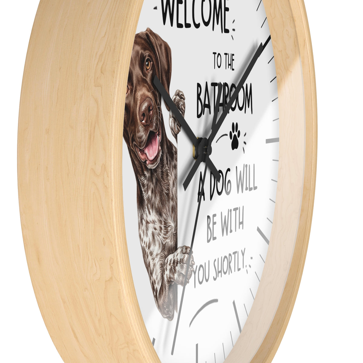 A round wall clock with a light natural wood frame and a white face. The clock features a German shorthaired pointer dog illustration on the left and black text that reads 'WELCOME TO THE BATROOM A DOG WILL BE WITH YOU SHORTLY'.