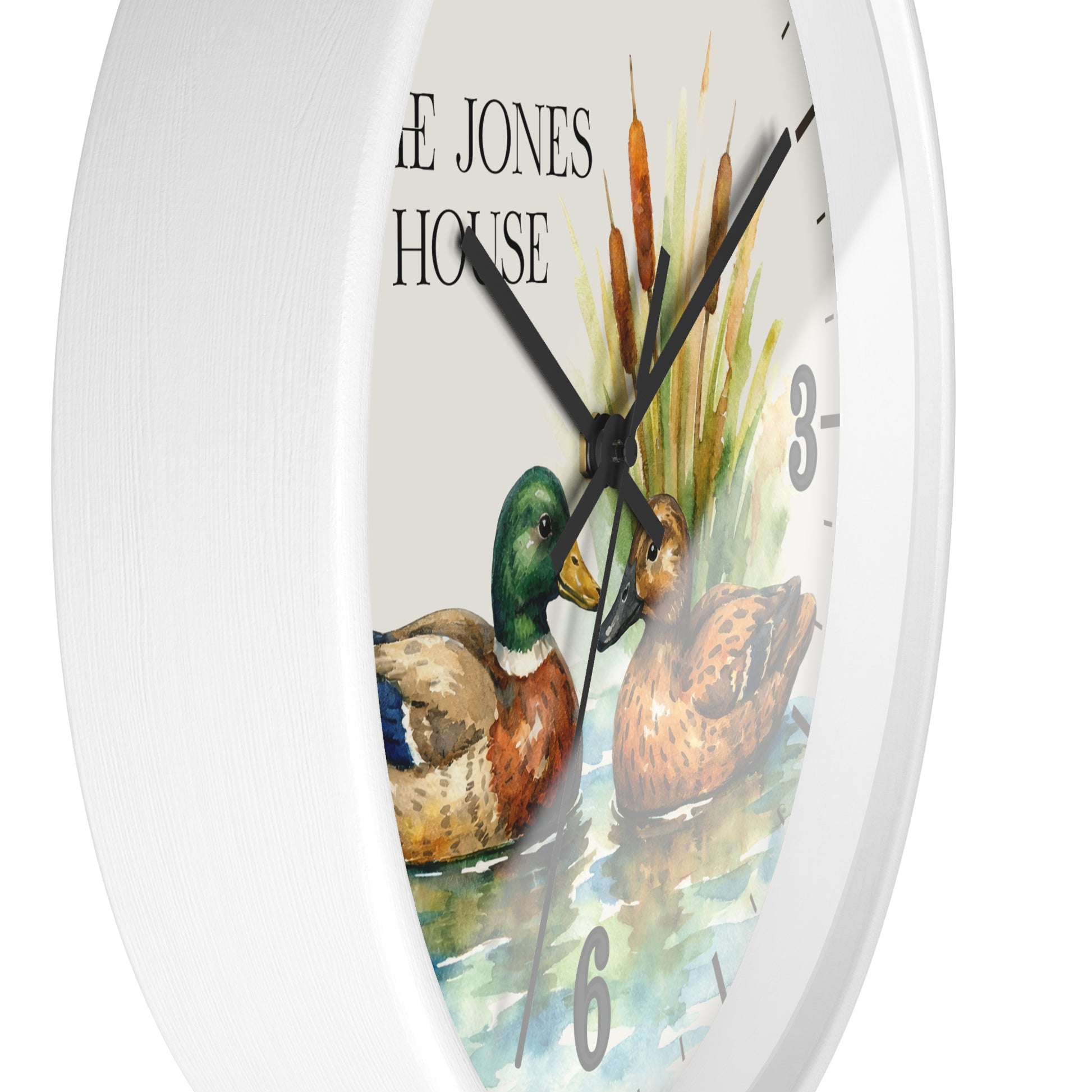 Round wall clock with a white frame and a watercolor-style duck illustration on the face, including a mallard duck, a brown duck, cattails, and the text 'THE JONES HOUSE'.