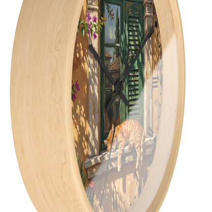 Round wall clock with a light natural wood frame and a printed scene of a ginger cat resting on a windowsill in front of a green shuttered door.