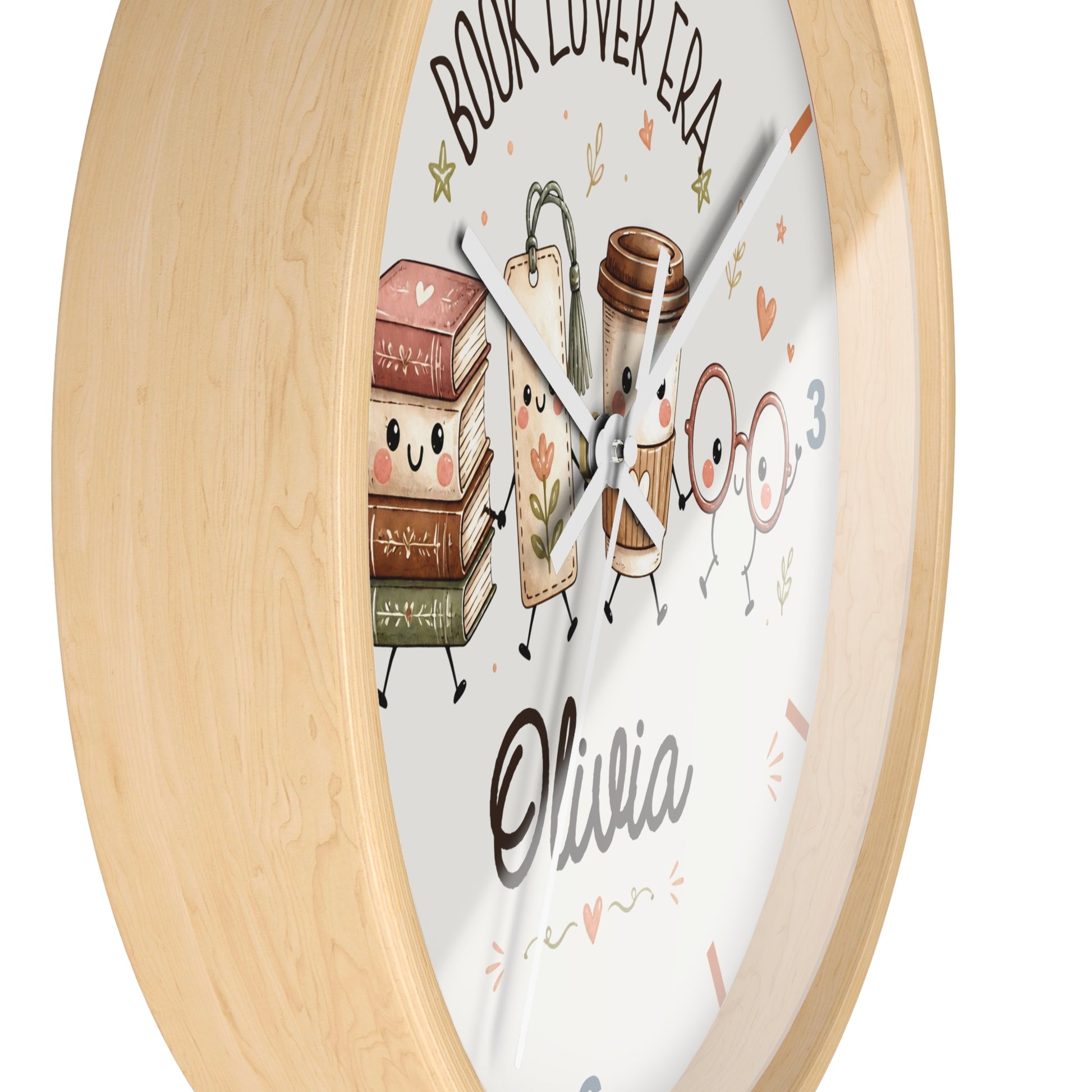 A round wall clock with a light natural wood frame and a white face featuring cute illustrated books, a coffee cup, glasses, and the words 'BOOK LOVER ERA' and the name 'Olivia'.