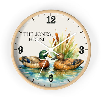 A round wall clock with a light wood frame and a watercolor-style duck scene on the face. The dial shows black Arabic numerals, white hands, cattails, reeds, and the text 'THE JONES HOUSE' near the 10 o'clock position.