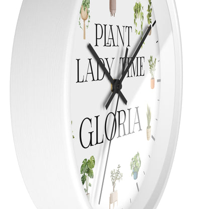A white round wall clock with black hands and the text 'PLANT LADY TIME GLORIA' printed on the face, decorated with small illustrated potted plants.