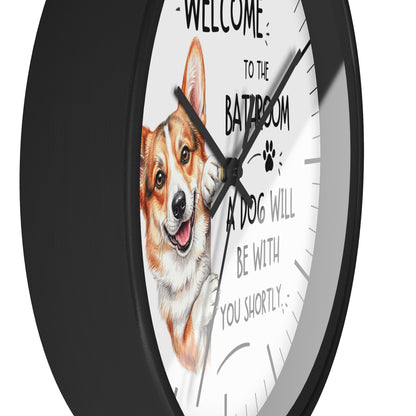 A round wall clock with a black frame and a white face, featuring a cartoon corgi illustration and the text 'WELCOME TO THE BATROOM A DOG WILL BE WITH YOU SHORTLY'.
