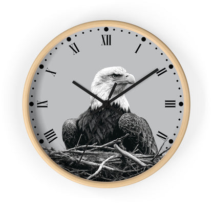Round wall clock with a light wood frame, black Roman numerals, and a grayscale photograph of a bald eagle sitting in a nest on the clock face, shown against a plain white background.