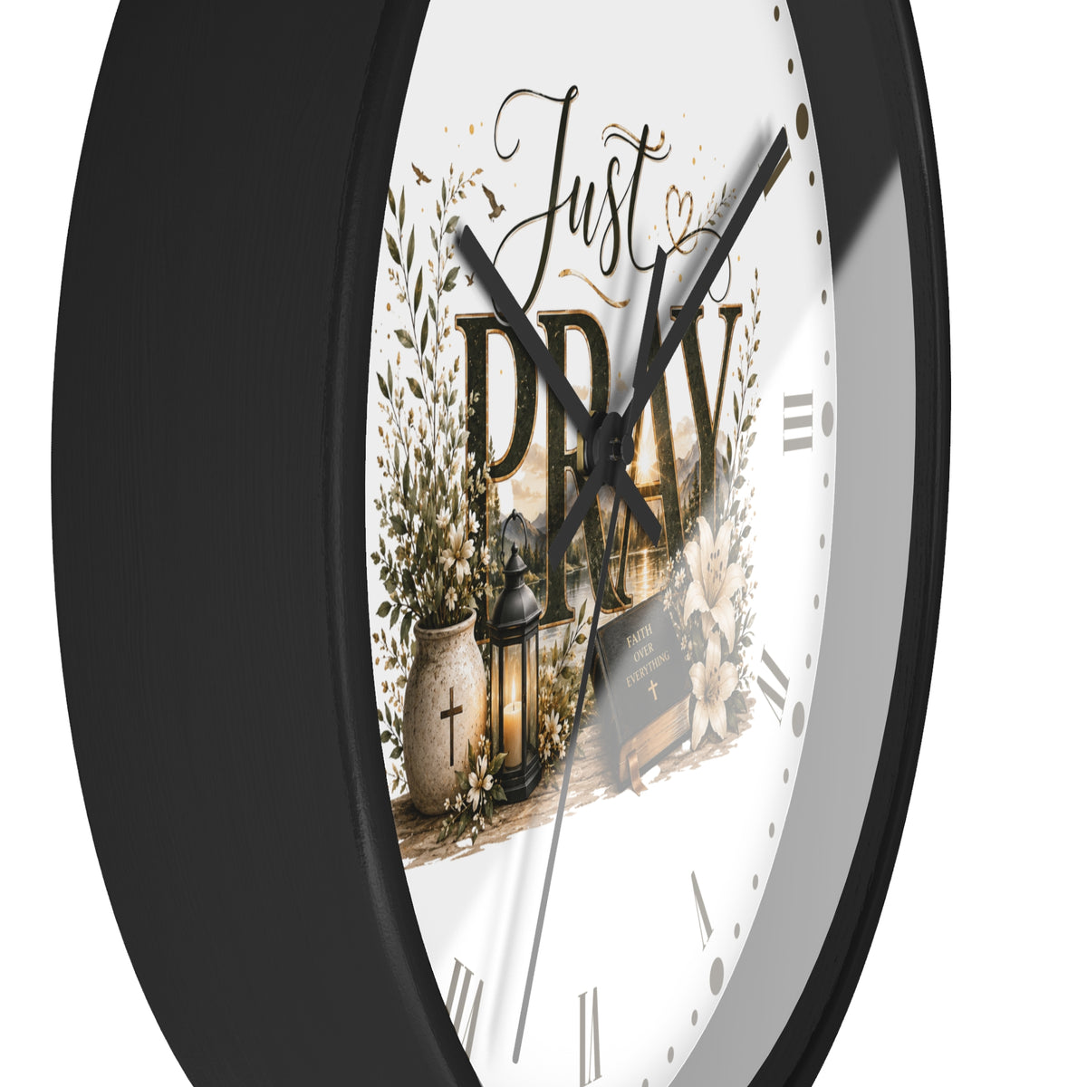 A close-up of a round wall clock with a black frame and a white face featuring the words 'Just PRAY' in script and block lettering, surrounded by decorative floral and lantern illustrations.