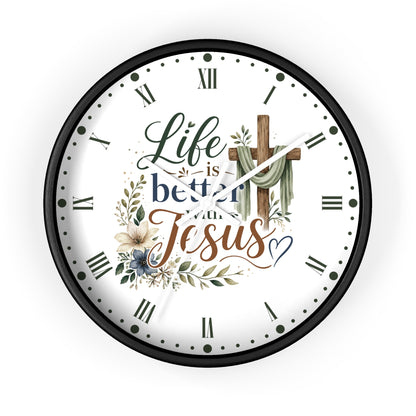 A round wall clock with a black frame and a white face featuring the text 'Life is better with Jesus' in decorative script, surrounded by floral and leaf illustrations and a wooden cross.