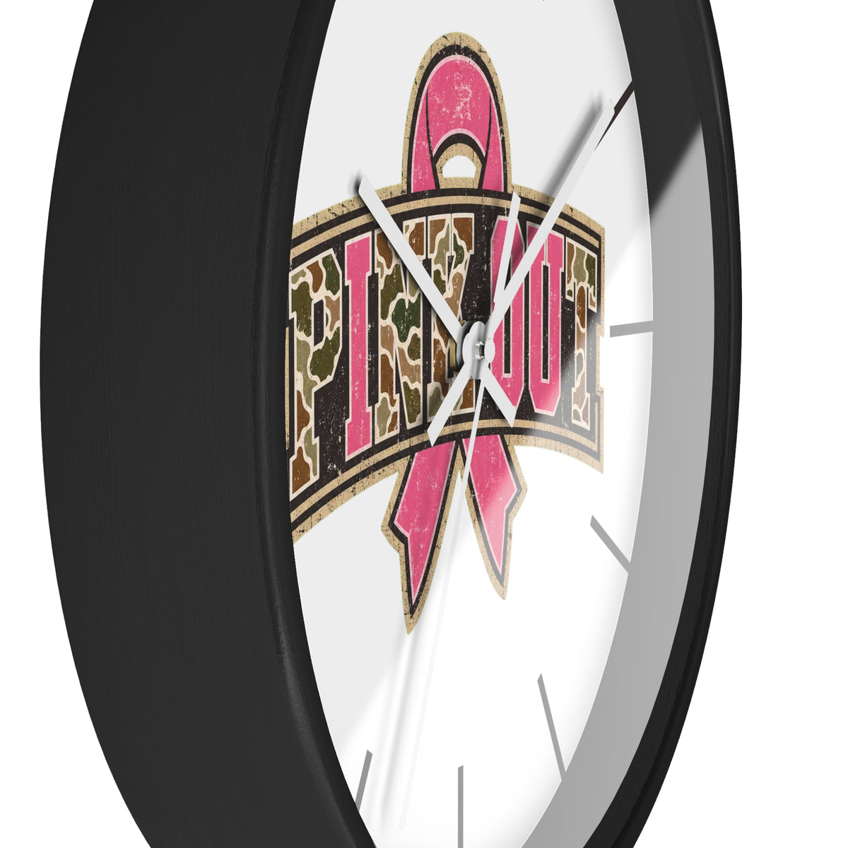 A close-up of a round wall clock with a black frame and a white face, featuring a large pink ribbon and camouflage-style text design on the front.