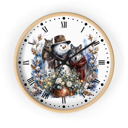A round wall clock with a light wood frame and a white face featuring a winter illustration of a snowman, a wolf, an owl, flowers, and snow-covered branches. The clock has black Roman numerals and black hands on a clean white background.
