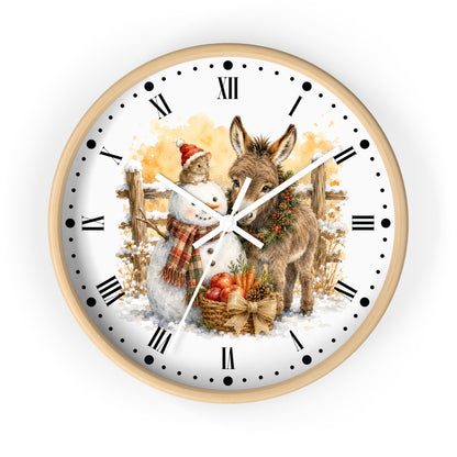 Round wall clock with a light wood frame and a white face featuring a winter holiday illustration of a snowman and a donkey, with black Roman numerals and hands on a white background.